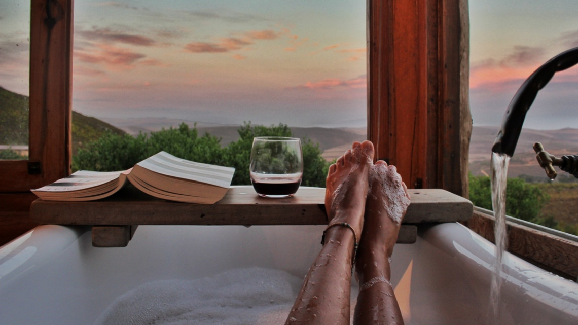 Photo of a woman's feet sticking out of a bath next to a drink and book